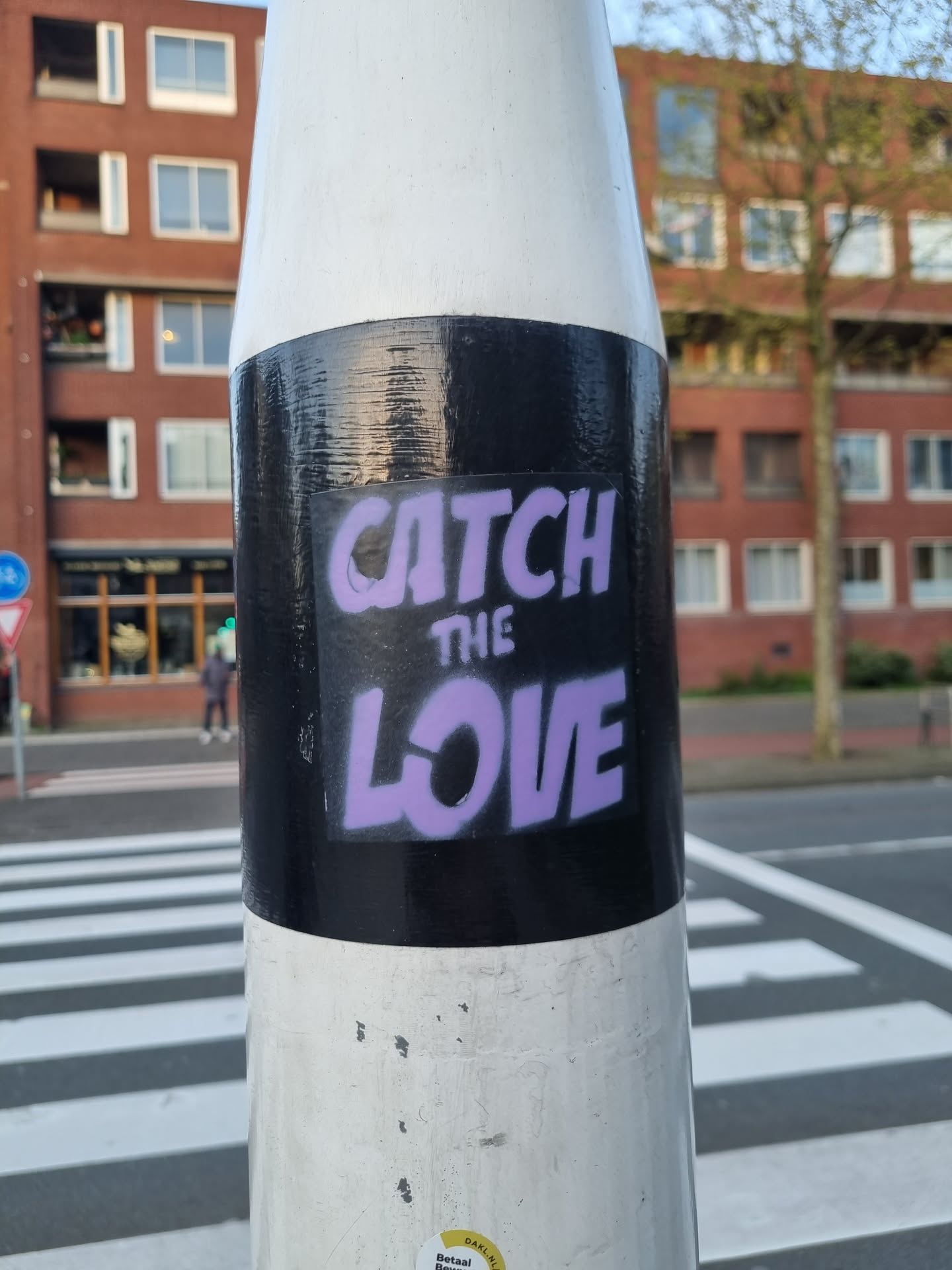 A purple and black sticker on a white pole with the text "CATCH THE LOVE". The sticker is placed on a black background.
