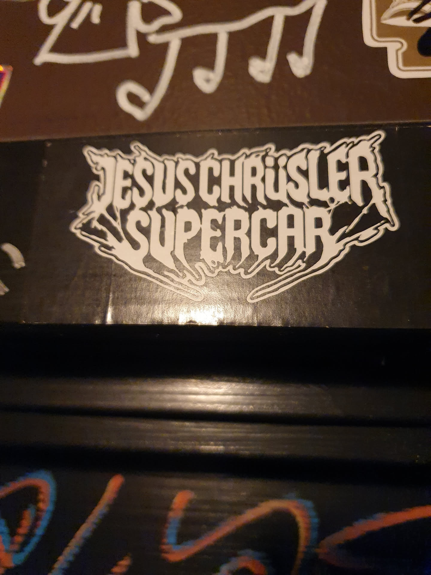 A black and white sticker with the text "JESUS CHRYSLER SUPERCAR" in a stylized font. The text appears to be in a gothic or metal style.