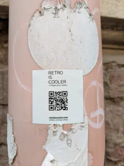 A square sticker on a light post with the text "Retro is cooler vintage story sellers" and a QR code. It also has the web address retroiscooler.com.