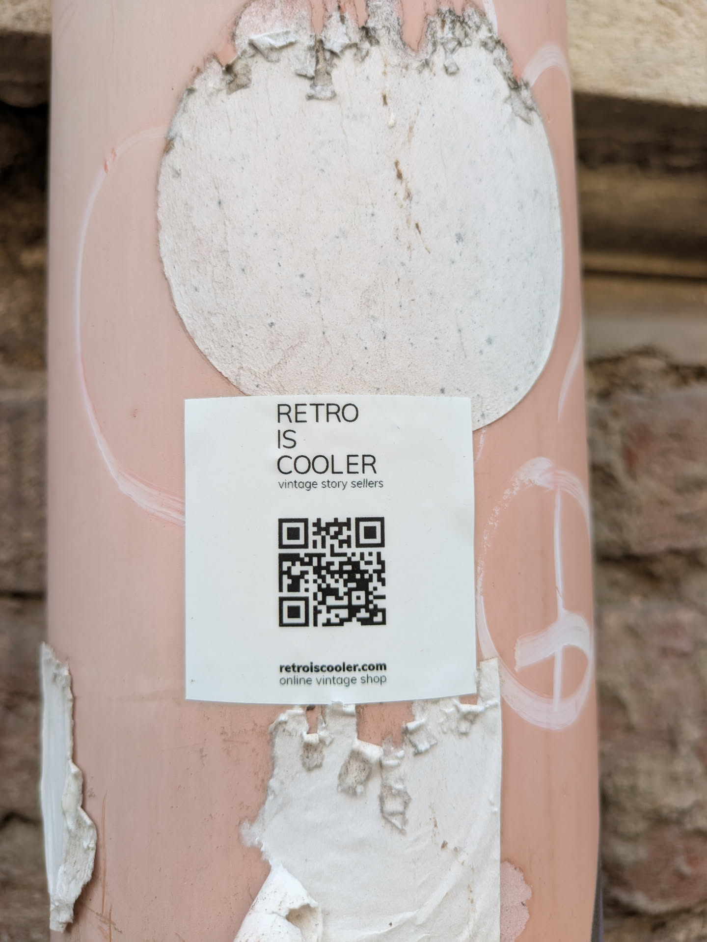 A square sticker on a light post with the text "Retro is cooler vintage story sellers" and a QR code. It also has the web address retroiscooler.com.