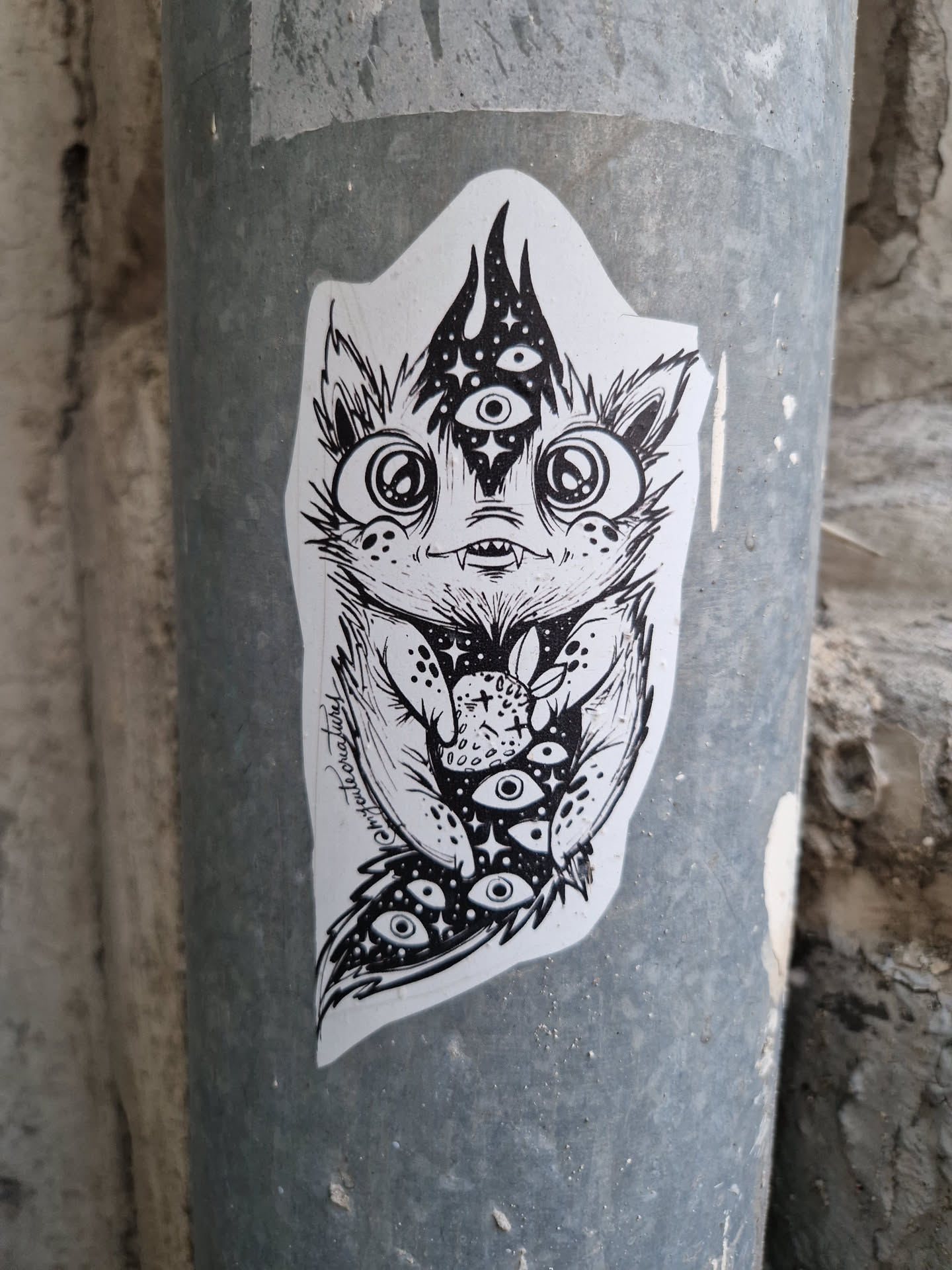 Black and white illustration of a cute monster cat holding a strawberry. It has multiple eyes and mystical vibes. The artwork is on a sticker.