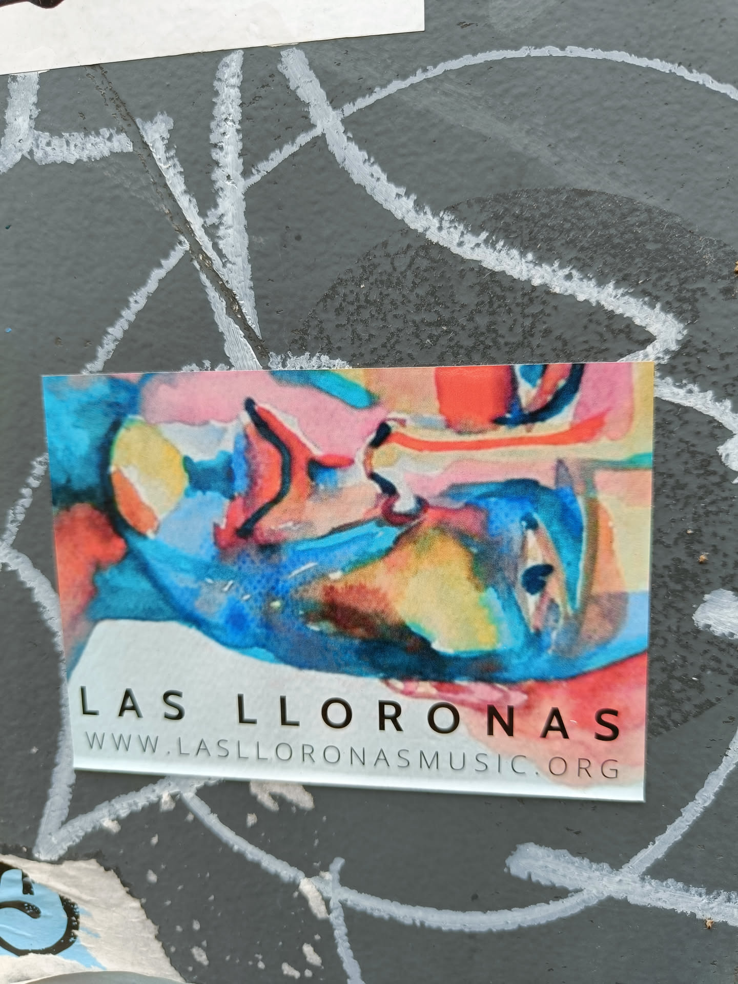 A watercolor-style sticker featuring an abstract face and the band's name and website.