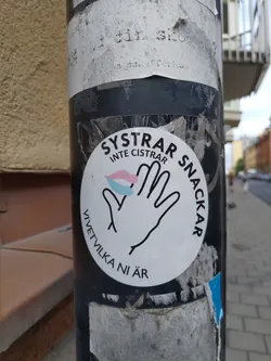 A white round sticker with black text and a graphic of a hand with a small pink, blue and white lips design. The text on the sticker says "SYSTRAR INTE CISTRAR SNACKAR" which translates to "Sisters don't silence, talk" and "VÄTVILKA NI ÄR" which translates to "who are you".