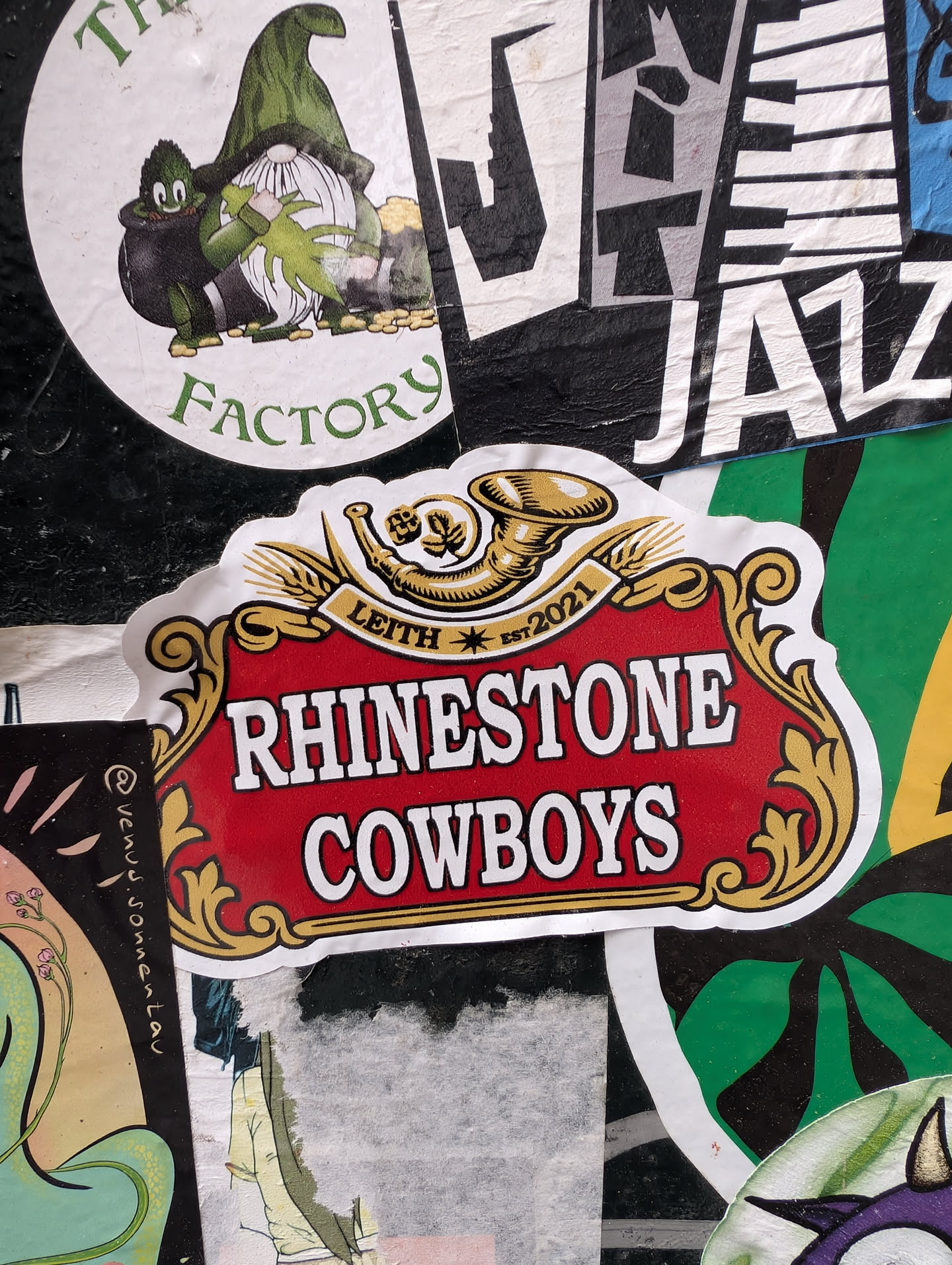 A rectangular sticker with a red background and ornate gold border. The sticker reads 'RHINESTONE COWBOYS' and 'LEITH EST. 2021' with a logo of a horn above the text.