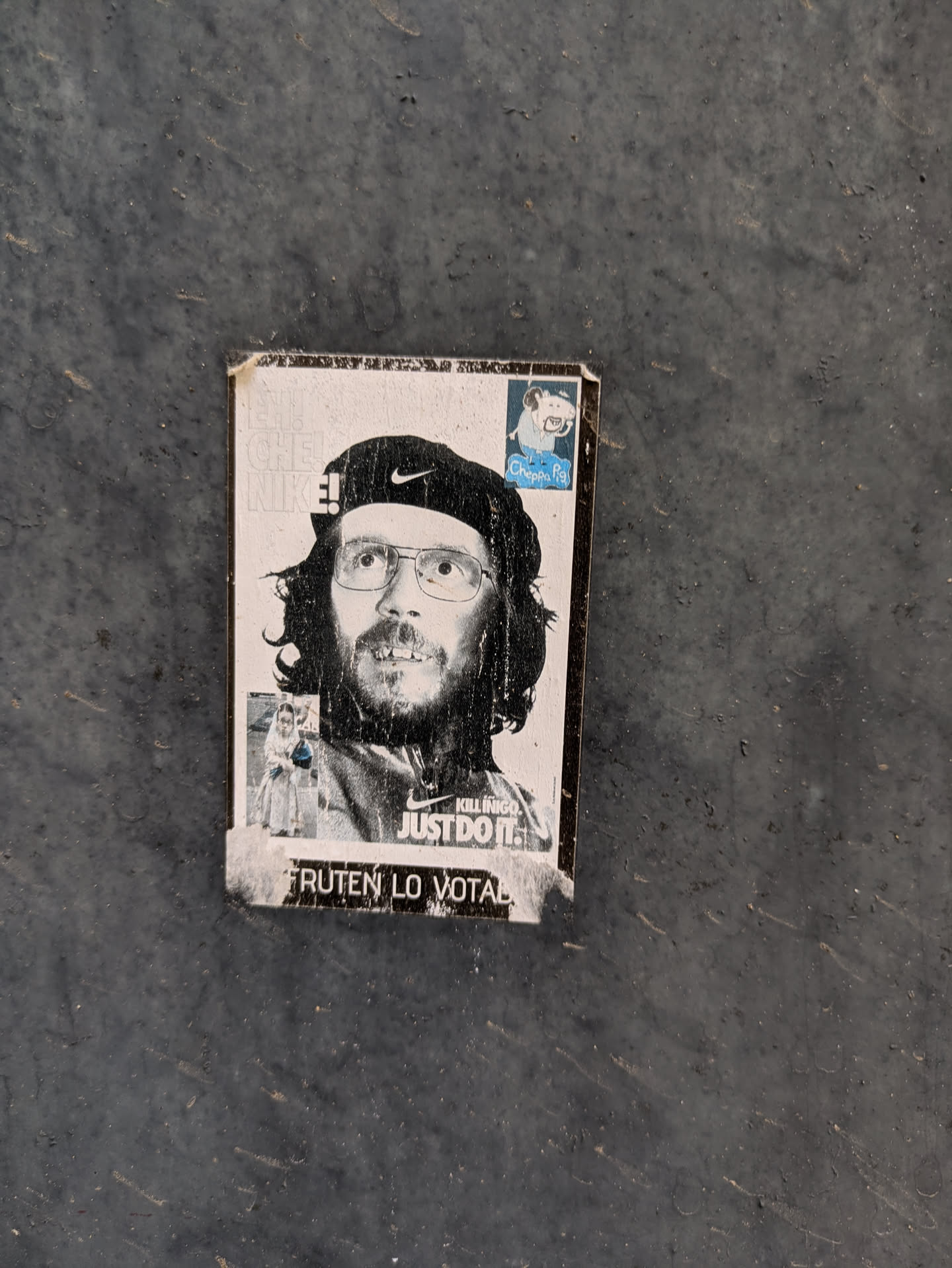 The sticker features a monochrome image of a man with a beard and glasses, wearing a beret with the Nike swoosh. Text on the sticker reads "CHE NIKE!" and "KILLINIGO. JUST DO IT."  It also says, 'FRUTEN LO VOTAN'. There is another sticker fragment on the top right that says 'Cheppa Pig'.