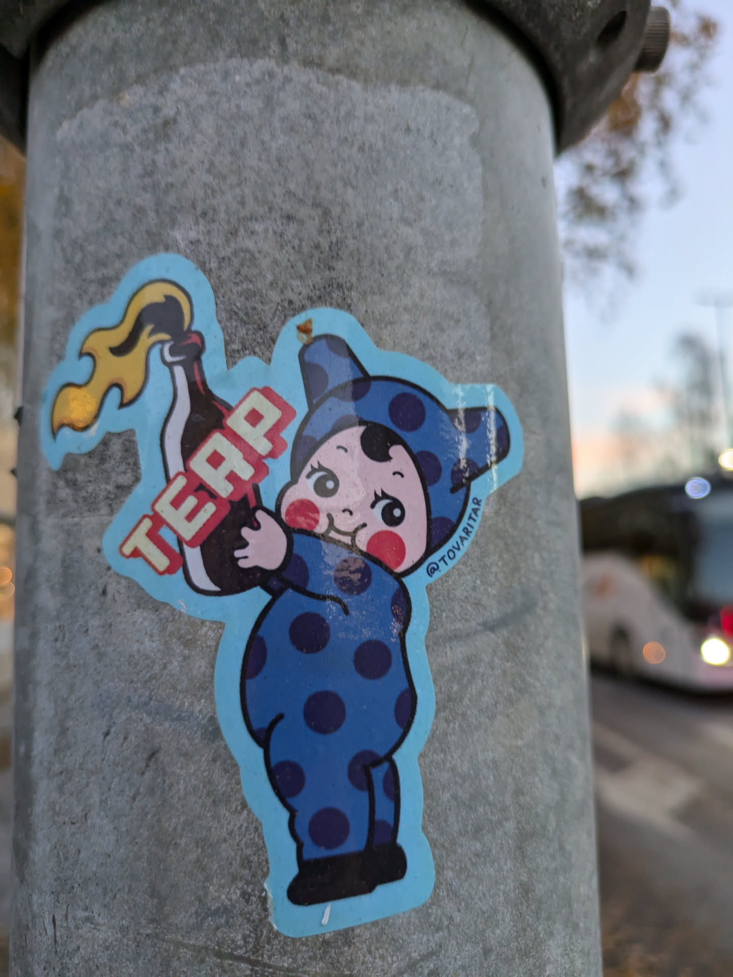 A sticker featuring a cartoon baby in a blue polka dot onesie holding a Molotov cocktail. The word "TEAP" is written on the cocktail bottle. The sticker is attached to a metal pole.