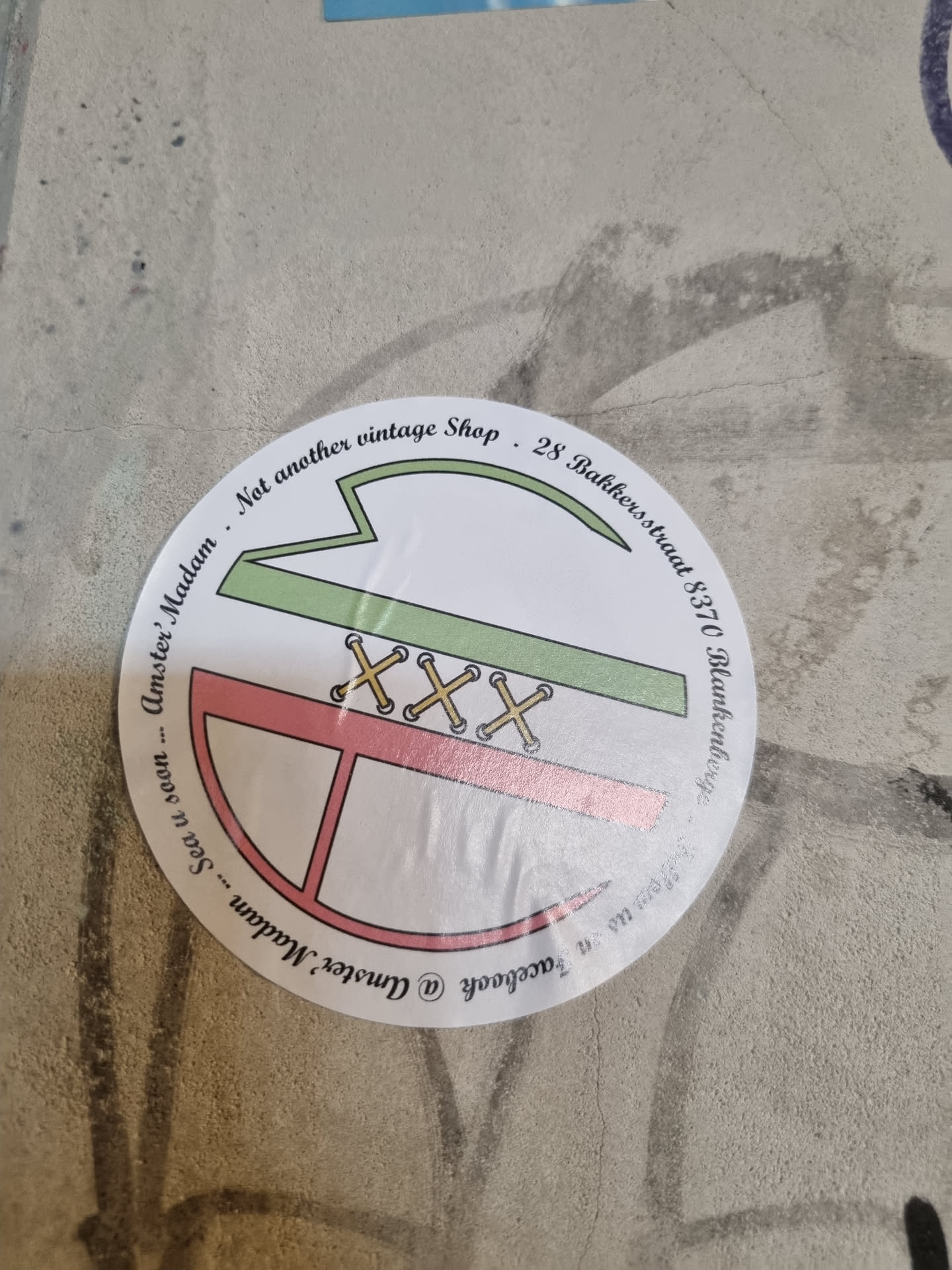 Round sticker with a minimalist design, featuring a map and the text 'Not another vintage shop'. The shop's address is written on the sticker, including the street name 'Bakkersstraat' and the city 'Blankenberge'.
