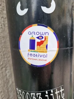 Round sticker with illustrations of a gas tank and a brick wall with an eye. The text 'Artown Festival' is at the top and bottom of the sticker. There is also a social media handle on the bottom of the sticker.