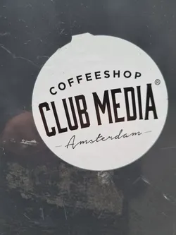 Round white sticker with black text. It says Coffeeshop Club Media Amsterdam. 