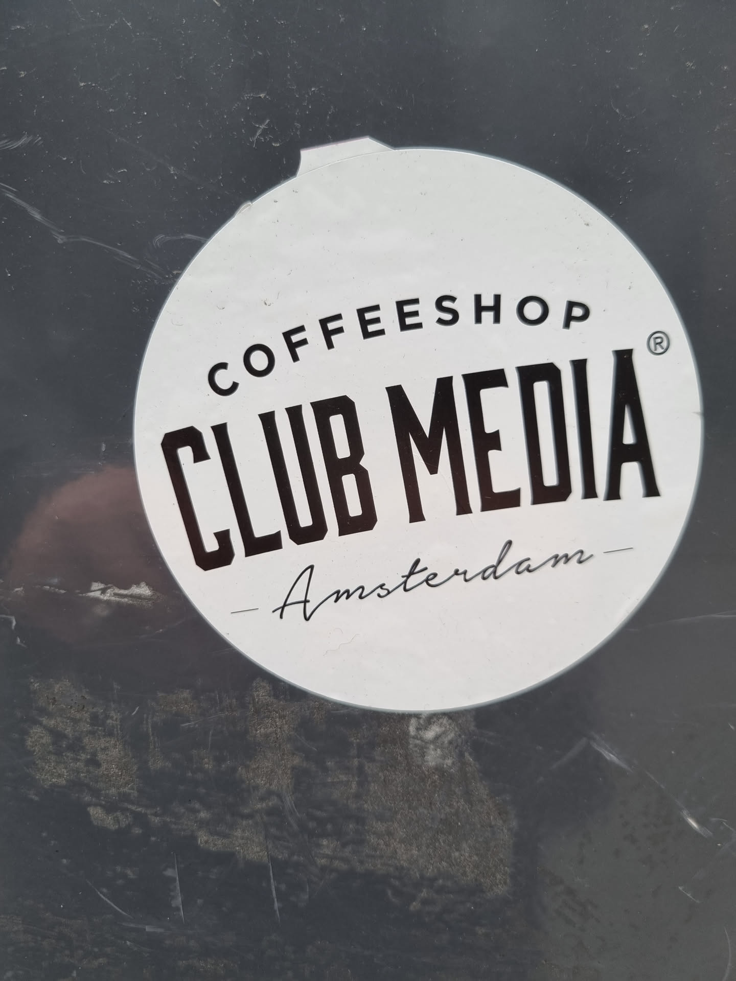 Round white sticker with black text. It says Coffeeshop Club Media Amsterdam. 