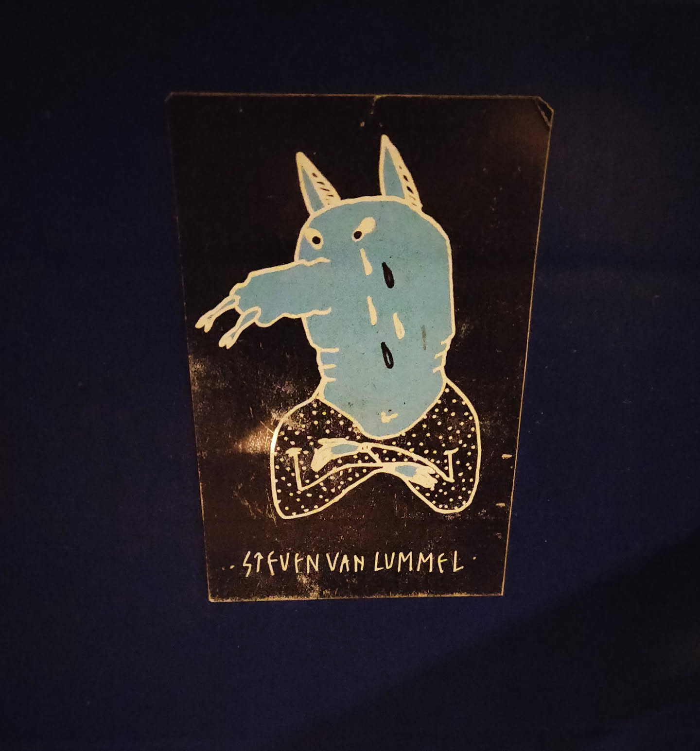 A sticker featuring a hand-drawn illustration of a blue creature with horns, seemingly sad, sitting with its arms crossed. The artwork is in a minimalist style with a dark background and light blue and white details. The artist's signature, "Steven van Lummel," is visible at the bottom.