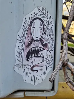 A sticker featuring No-Face from Spirited Away, holding a cute cat. The art style is dark, whimsical and detailed, with a touch of gothic flair. The sticker has a dripping effect at the bottom and some small stars surrounding the main characters. The artist's signature is visible at the bottom.