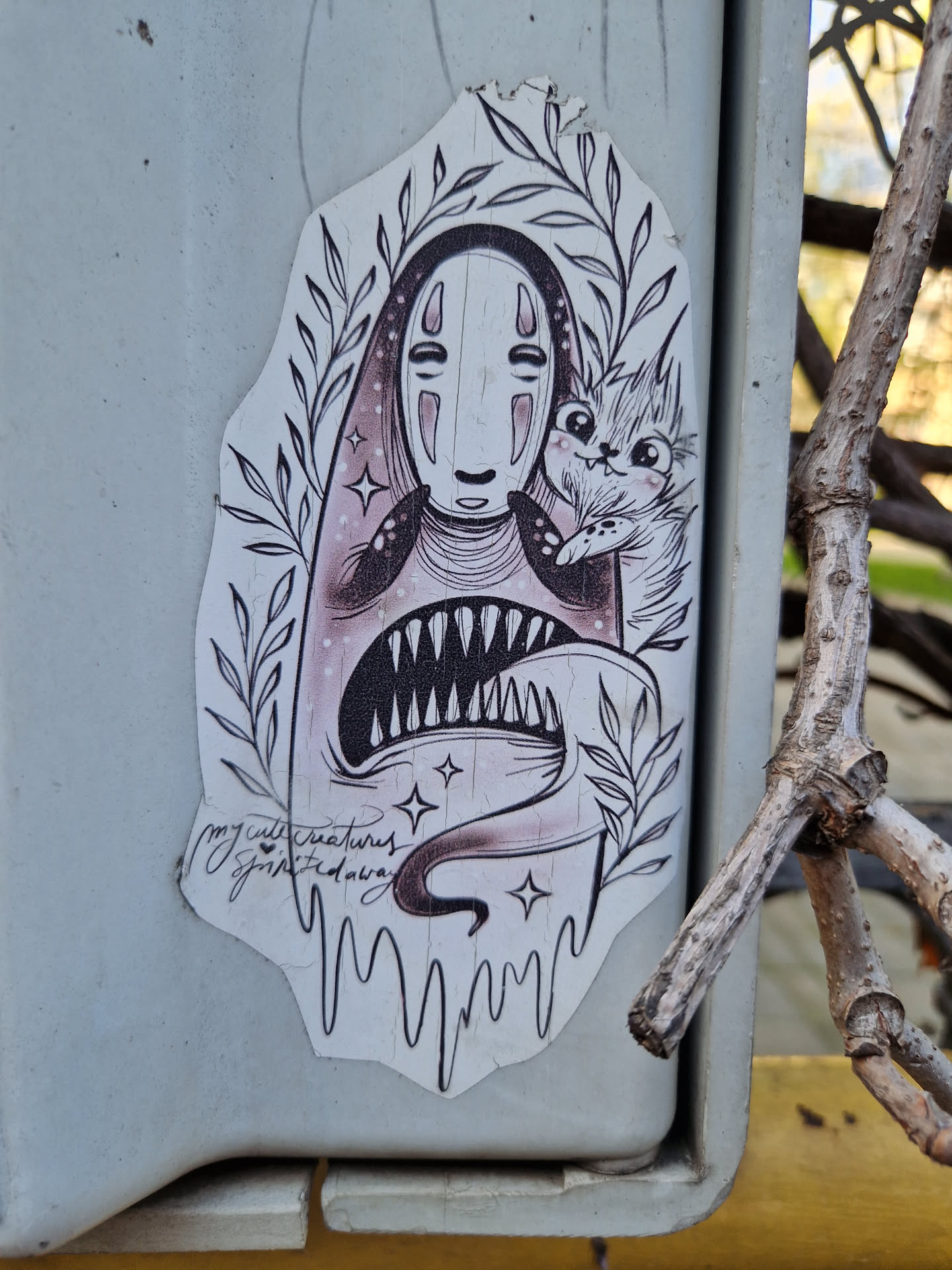 A sticker featuring No-Face from Spirited Away, holding a cute cat. The art style is dark, whimsical and detailed, with a touch of gothic flair. The sticker has a dripping effect at the bottom and some small stars surrounding the main characters. The artist's signature is visible at the bottom.