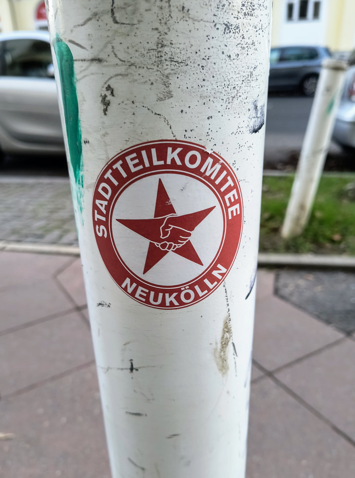 A red and white sticker with a red star and clasped hands in the center. The text around the star says "Stadtteilkomitee Neukölln".
