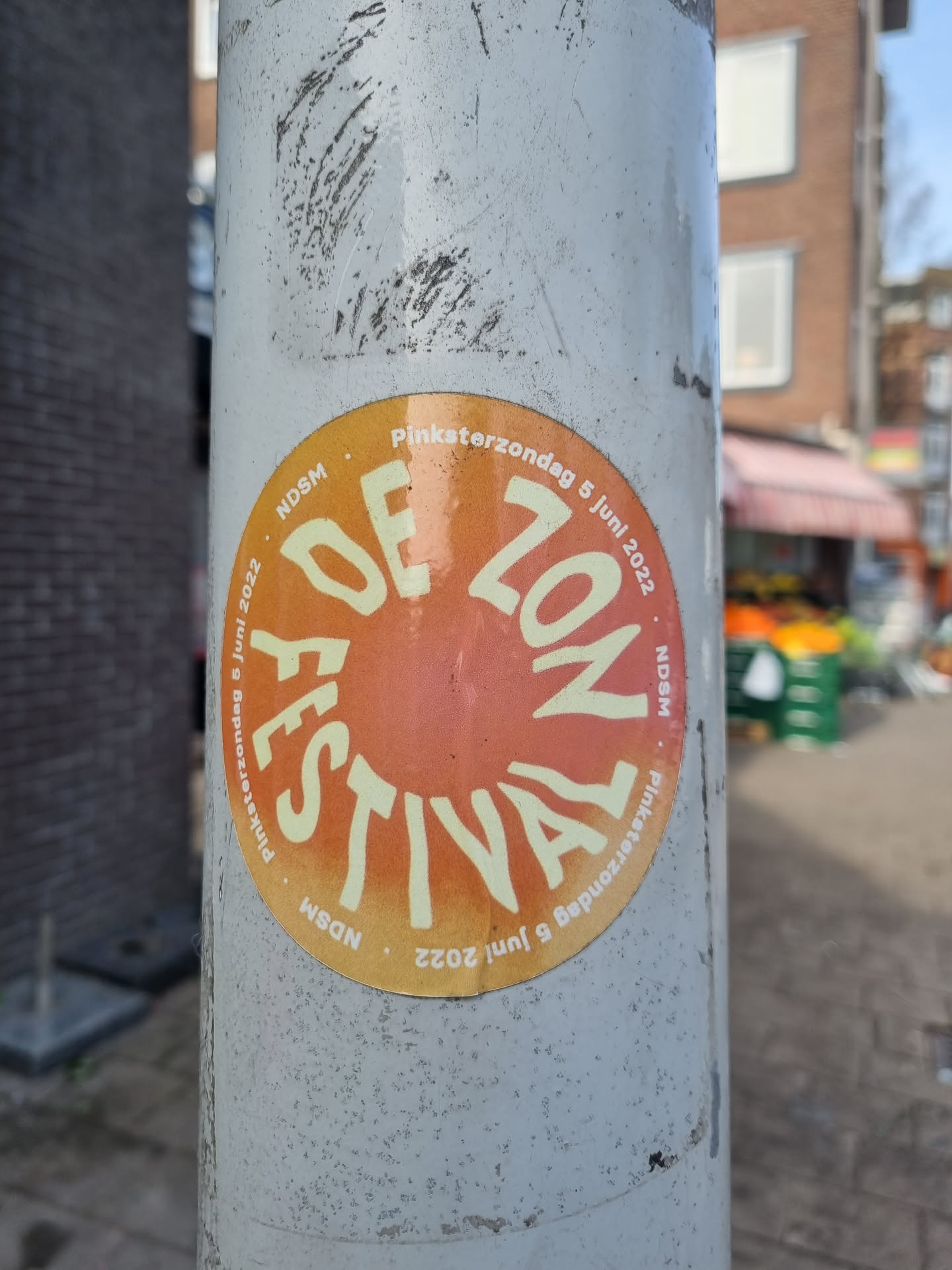 A round sticker advertising the De Zon Festival, held on Whit Sunday (Pinksterzondag), June 5th, 2022, in NDSM.  The design features a sunburst and the festival's name in a stylized font.
