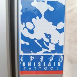 A blue and white sticker with an abstract design and the text "GHISLAIN TATTOOS" in a stylized font. There are also some Chinese characters above the name.
