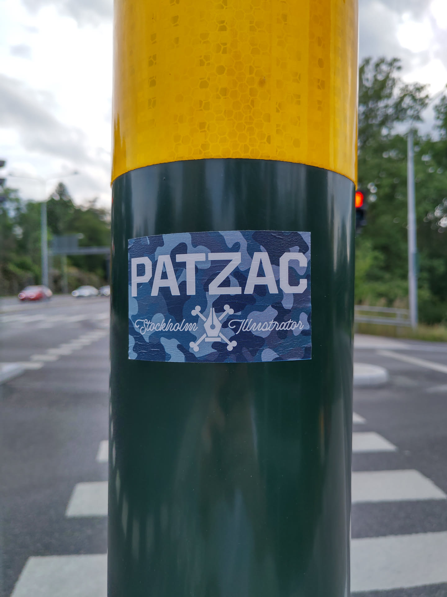 A sticker featuring the artist's name PATZAC, their location (Stockholm), and the word Illustrator.  The design incorporates a camouflage pattern and a simple illustration of a pen and crossbones. 