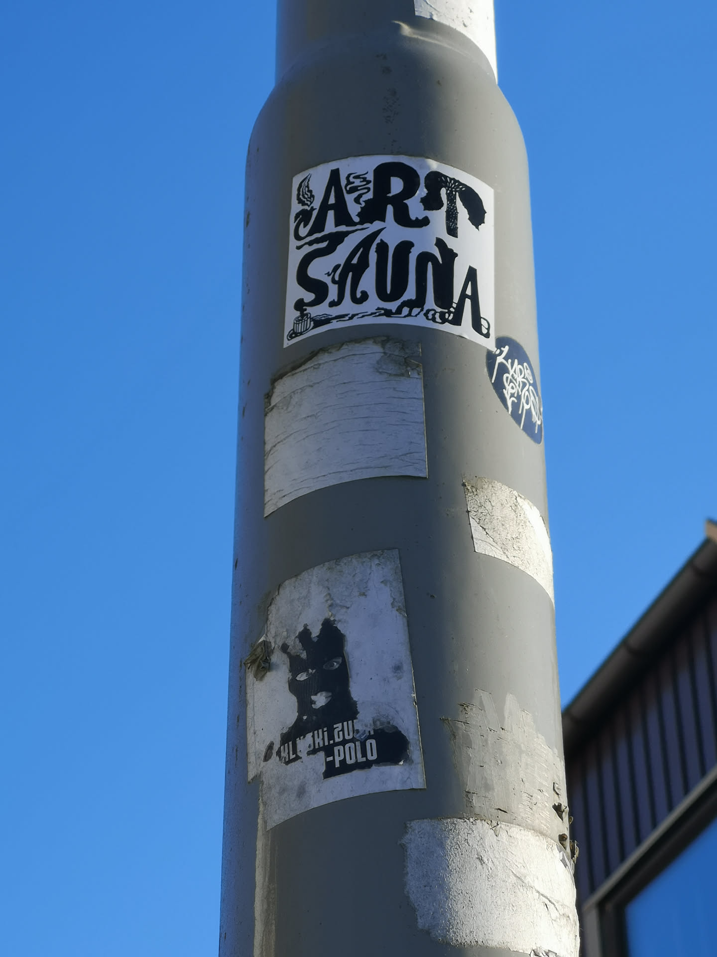The central sticker is a rectangular, black-on-white design featuring the words 'ART SAUNA' in a highly stylized, illustrative font. The letters of 'ART' are intricately designed, with the 'A' incorporating a flame or smoke motif and the 'T' forming a silhouette of a figure. The letters of 'SAUNA' have a fluid, organic, almost steam-like or wavy appearance. Below the 'S' in 'SAUNA', a small, detailed illustration of a sauna bucket and ladle is visible. The overall aesthetic is a blend of bold typography and intricate line art, giving it a distinctive, somewhat whimsical, and dark graphic novel feel.