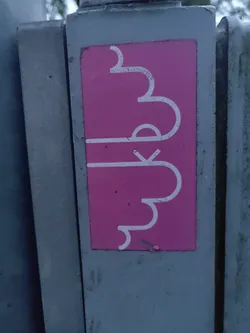 A pink sticker with a white abstract design is affixed to a gray metal surface. The design is composed of curved lines forming an organic shape.  The sticker shows slight wear.