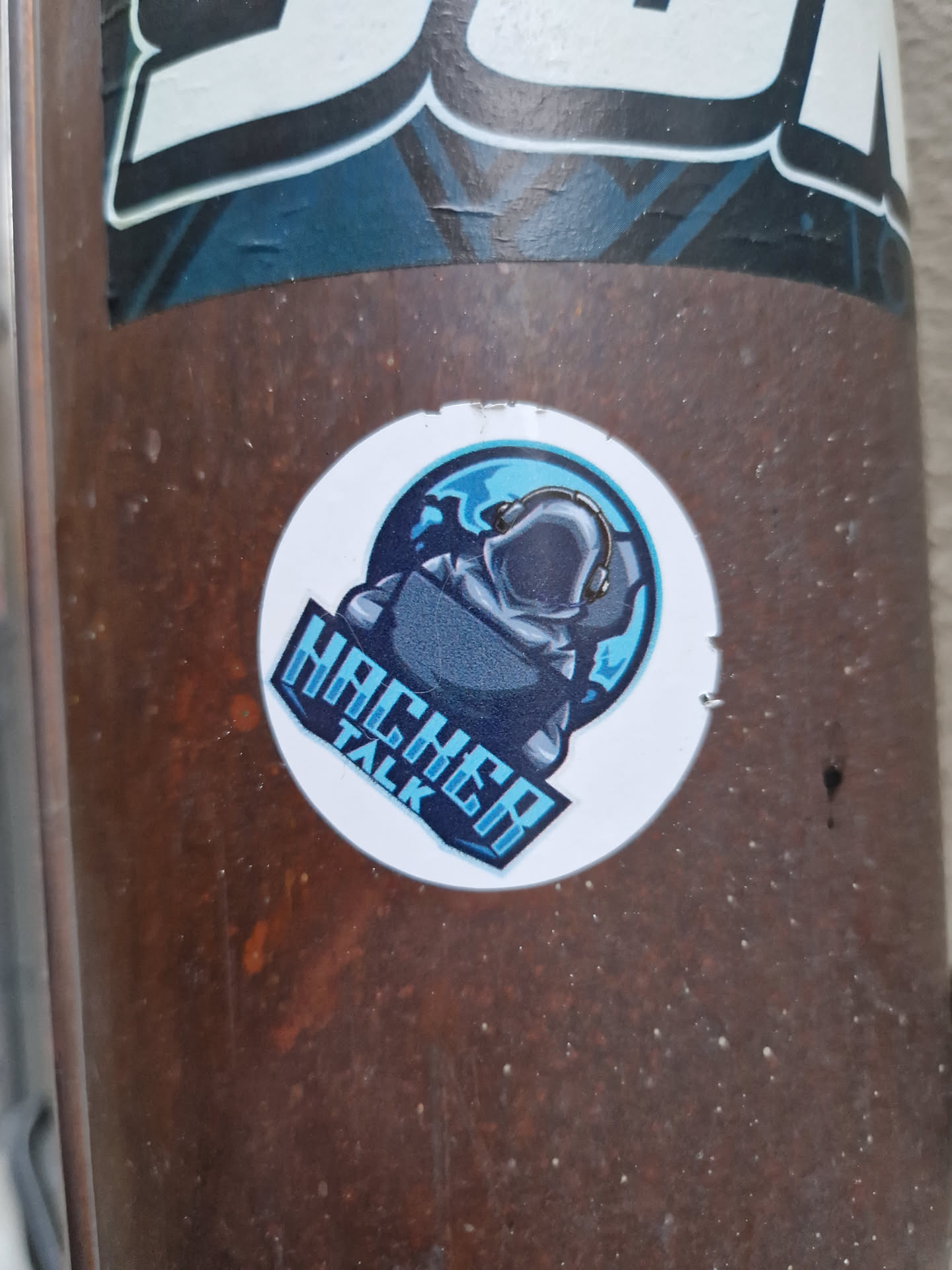 A round sticker featuring a logo of a hooded figure sitting in front of a laptop with a globe in the background. The text "Hacker Talk" is written vertically on the sticker.