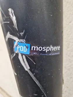 A sticker for mosphere, a podcast platform, stuck on a dark grey pole. The sticker is slightly worn and has some scratches.