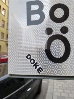 A black and white sticker with the word DOKE written in a stylized font. It's been placed on a reflective surface with black lettering. 
