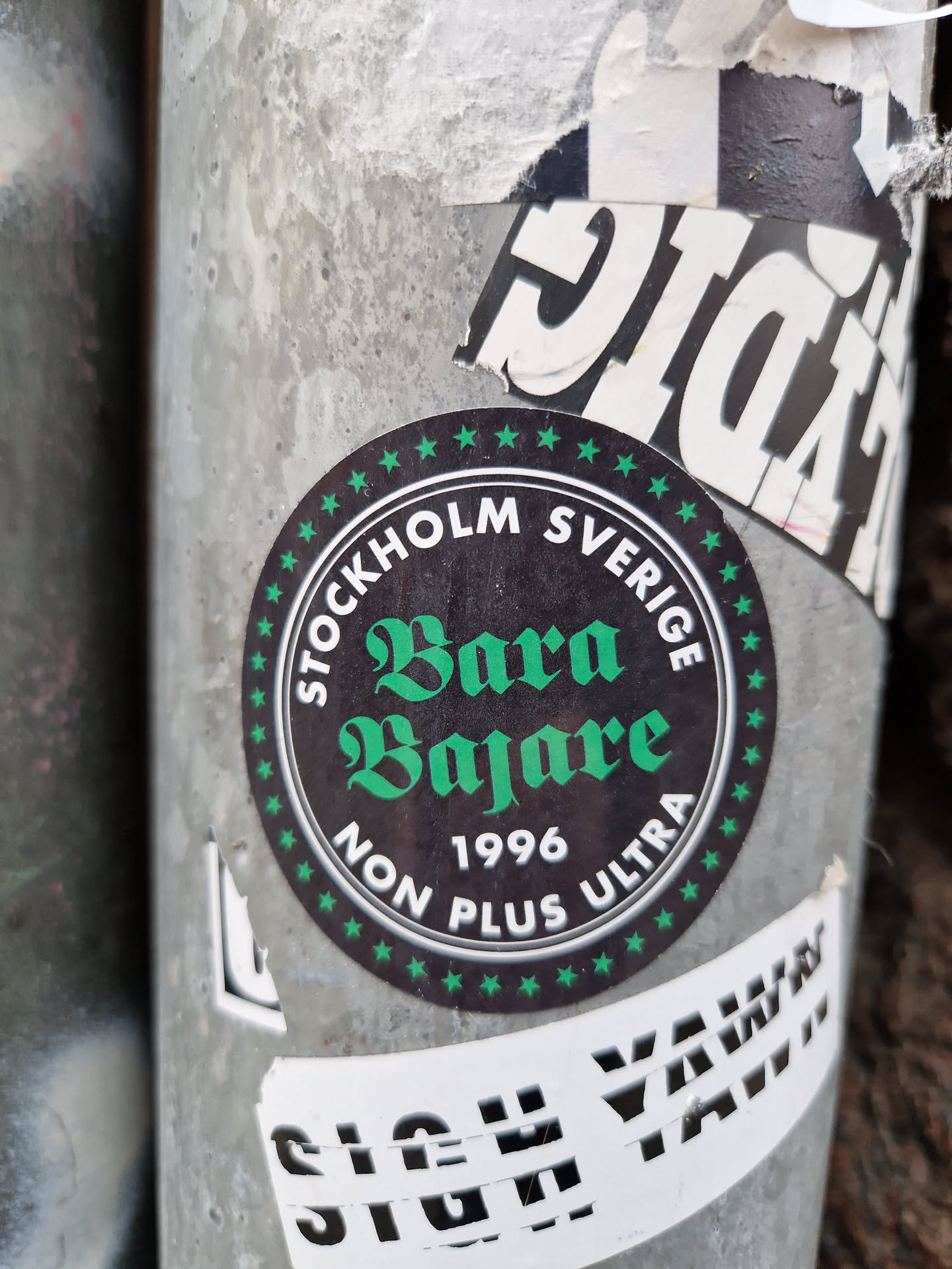 Round black and green sticker with the text "STOCKHOLM SVERIGE" on the top and bottom, "Bara Bajare" in the center, and "1996 NON PLUS ULTRA" below it. The text is written in a stylized font.