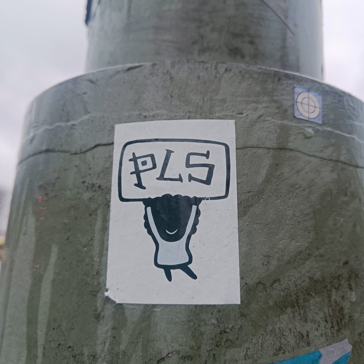 A sticker featuring a simple cartoon drawing of a person holding a sign that says "PLS". The drawing is in black and white and has a minimalist style.