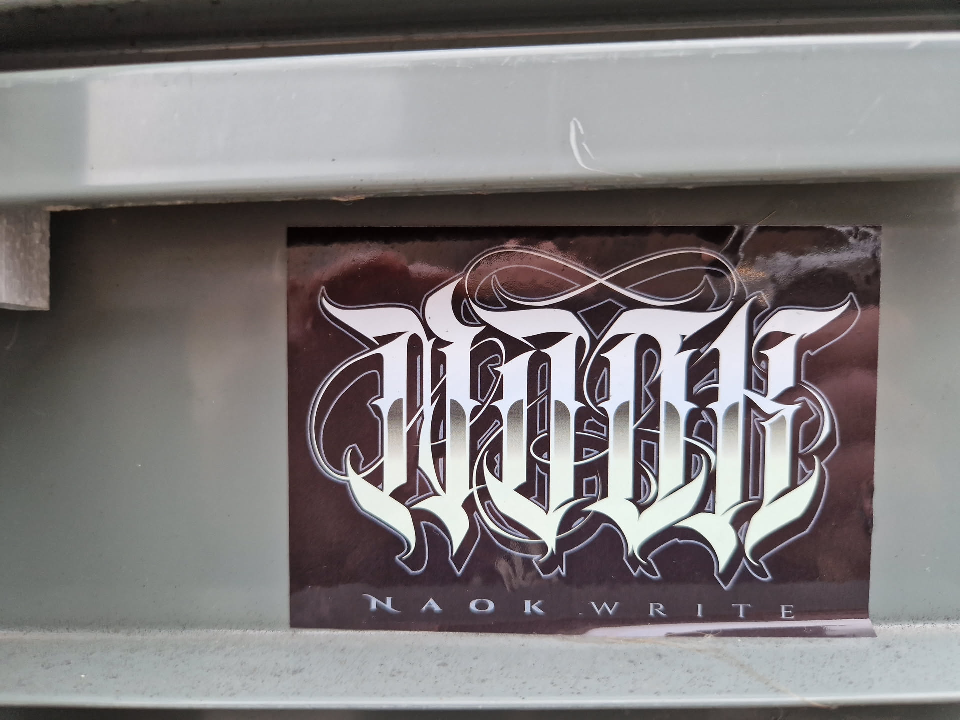 A sticker with a stylized logo of the text "NAOK WRITE" in silver on a dark background.
