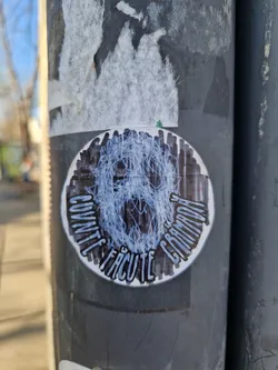 A round sticker with a dark background features a light blue, tangled, abstract figure in the center. The text "Cuvinte făcute grimadă" is written around the figure in a handwritten-style font. The sticker has a worn and distressed appearance.