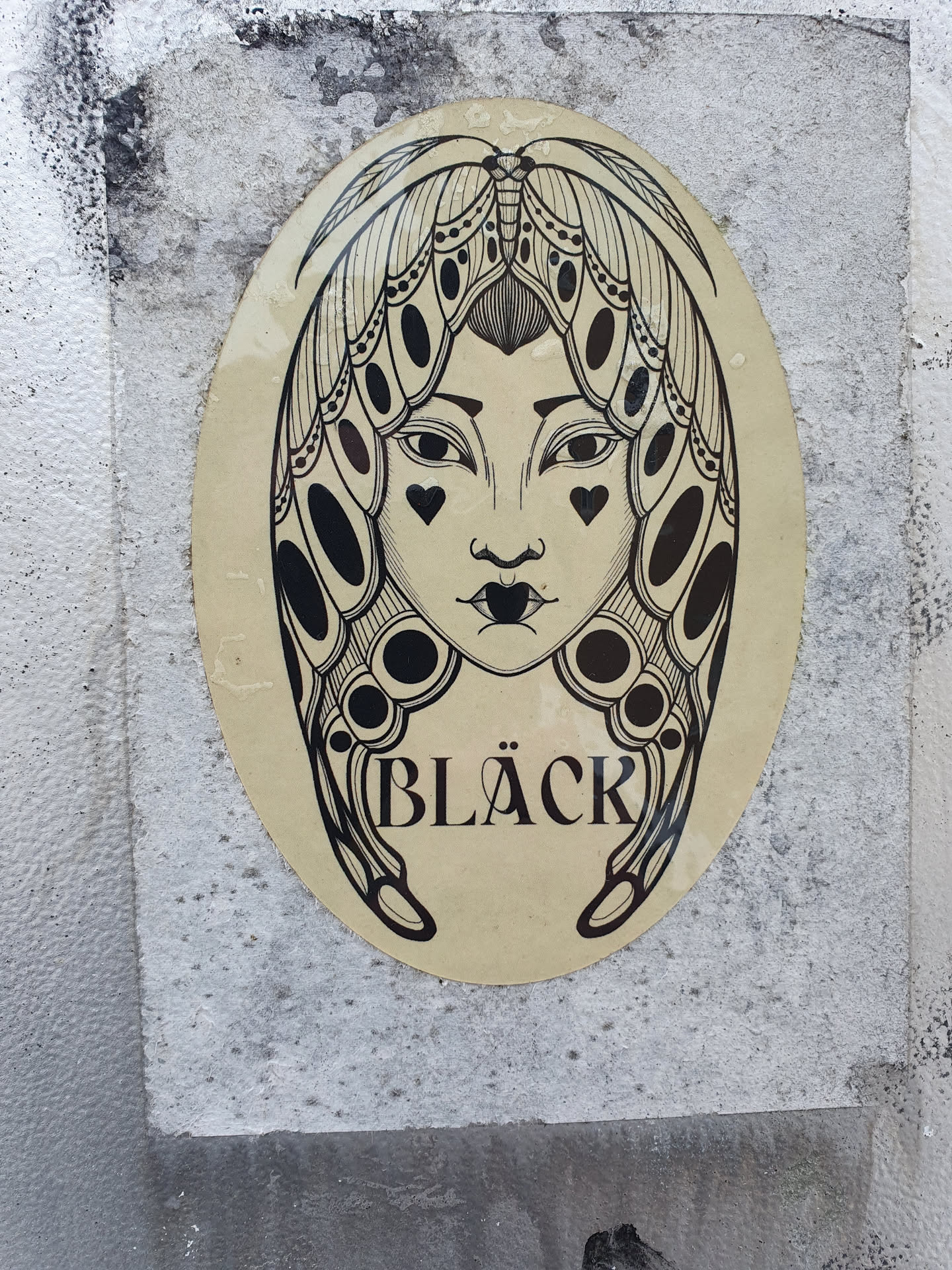 Oval sticker featuring a monochrome illustration of a woman's face framed by moth wings. The word "BLACK" is written at the bottom. The style is reminiscent of tattoo art.