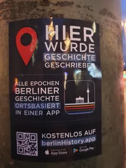 This sticker promotes the berlinHistory app, a location-based app that showcases the history of Berlin.  The text on the sticker says, "Here history was written." and it features a QR code linking to the app's download pages.