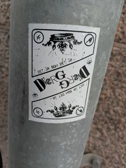 This sticker shows a monochrome design with a crown as a central element. The text "DET ÄR SOM DET ÄR..." is repeated vertically on both sides of the crown. There are also additional symbols, likely adding to the visual message or brand.