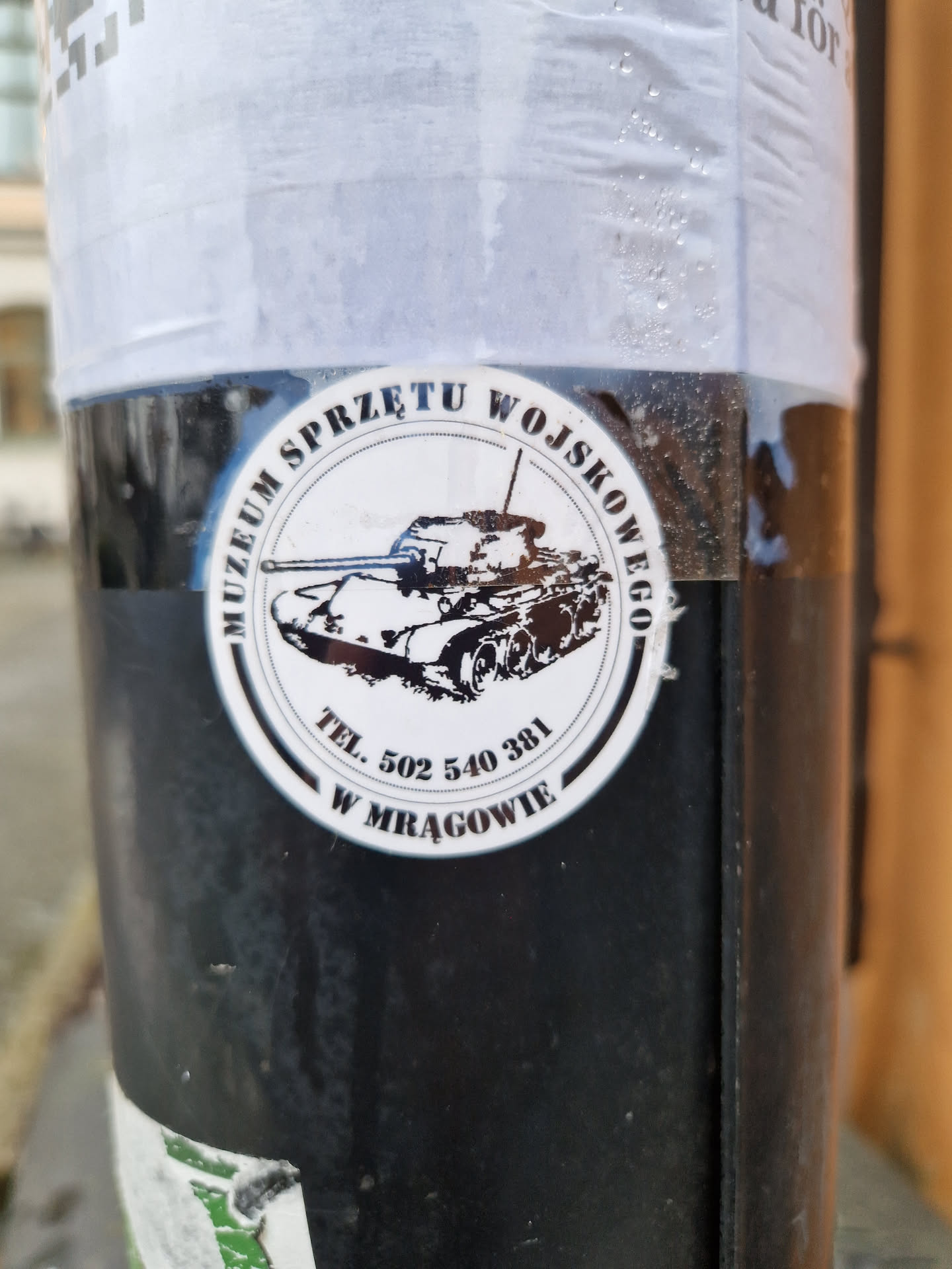 A round sticker featuring a tank and the text: "MUZEUM SPRZĘTU WOJSKOWEGO TEL. 502 540 381 W MRĄGOWIE"