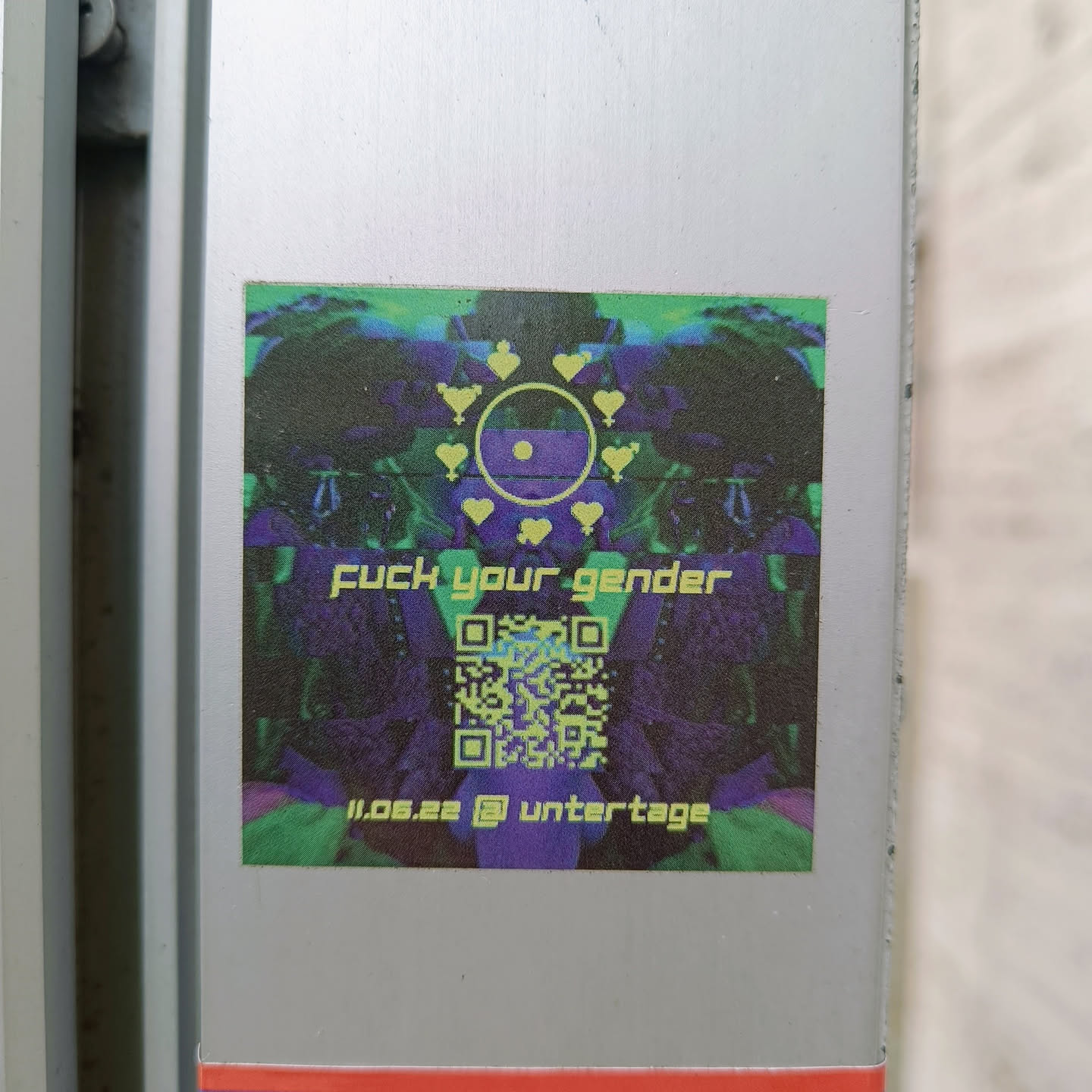 A square sticker with a psychedelic design. It features a central symbol surrounded by hearts and gender symbols. At the bottom, there is a QR code and the text "11.06.22 @ untertage".