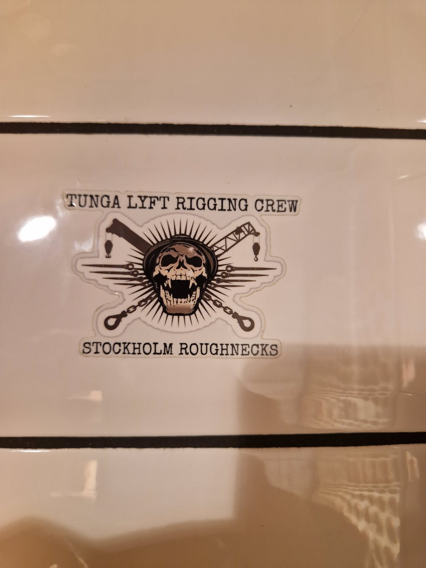 Sticker featuring a skull design with rigging and crane imagery. The text 'Tunga Lyft Rigging Crew' and 'Stockholm Roughnecks' is visible. 