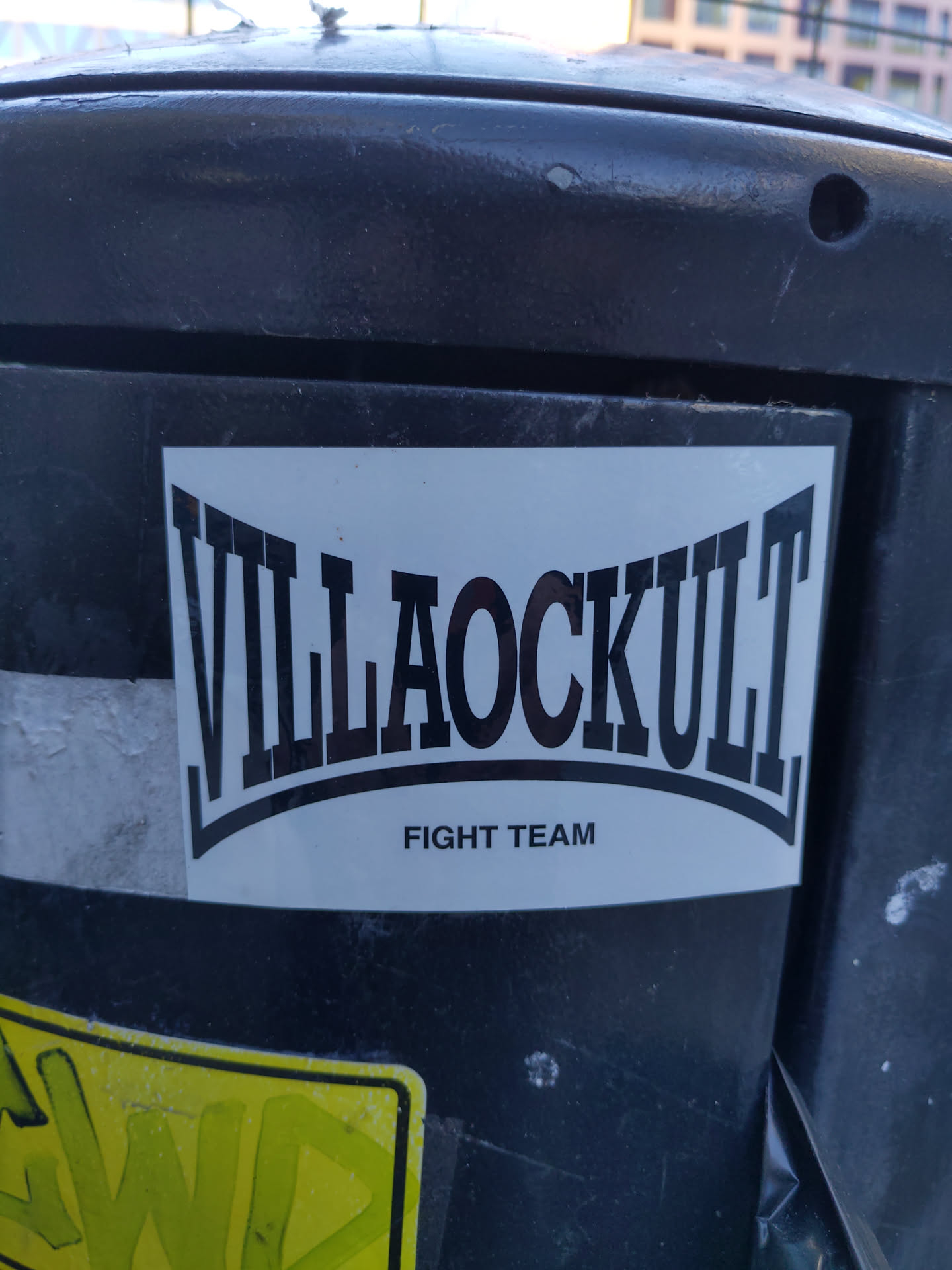 A sticker featuring the text "Villaockult" in a stylized font, with the words "Fight Team" written below it. The sticker is white with black text and is affixed to a dark-colored surface.