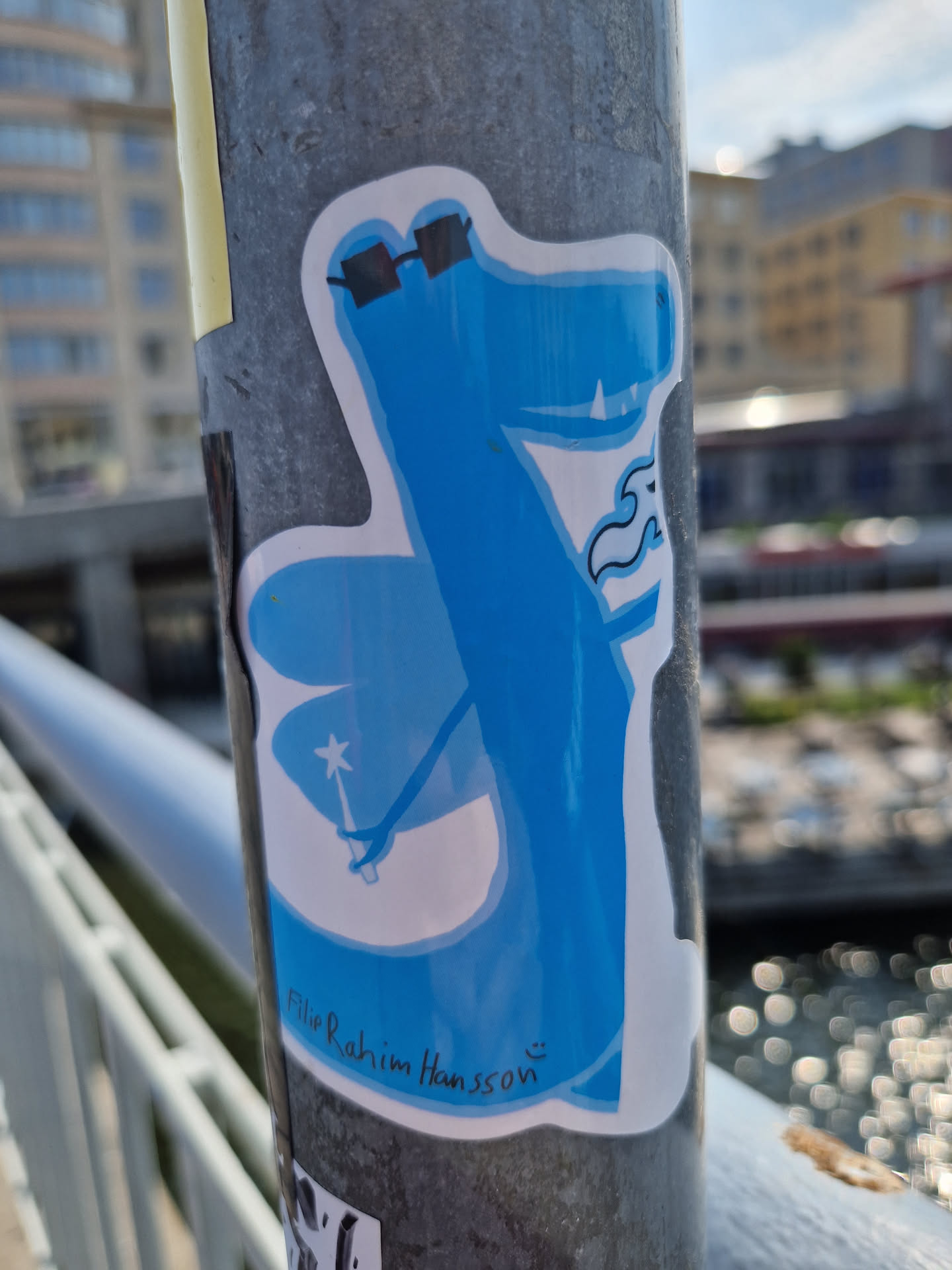 A light blue dragon wearing glasses and holding a magic wand. The artist's signature is visible at the bottom: "Filipe Rahim Hansson".
