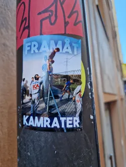 A sticker featuring a photo of people playing soccer, with the words "FRAMÅT" at the top and "KAMRATER" at the bottom. The overall style is reminiscent of street photography.