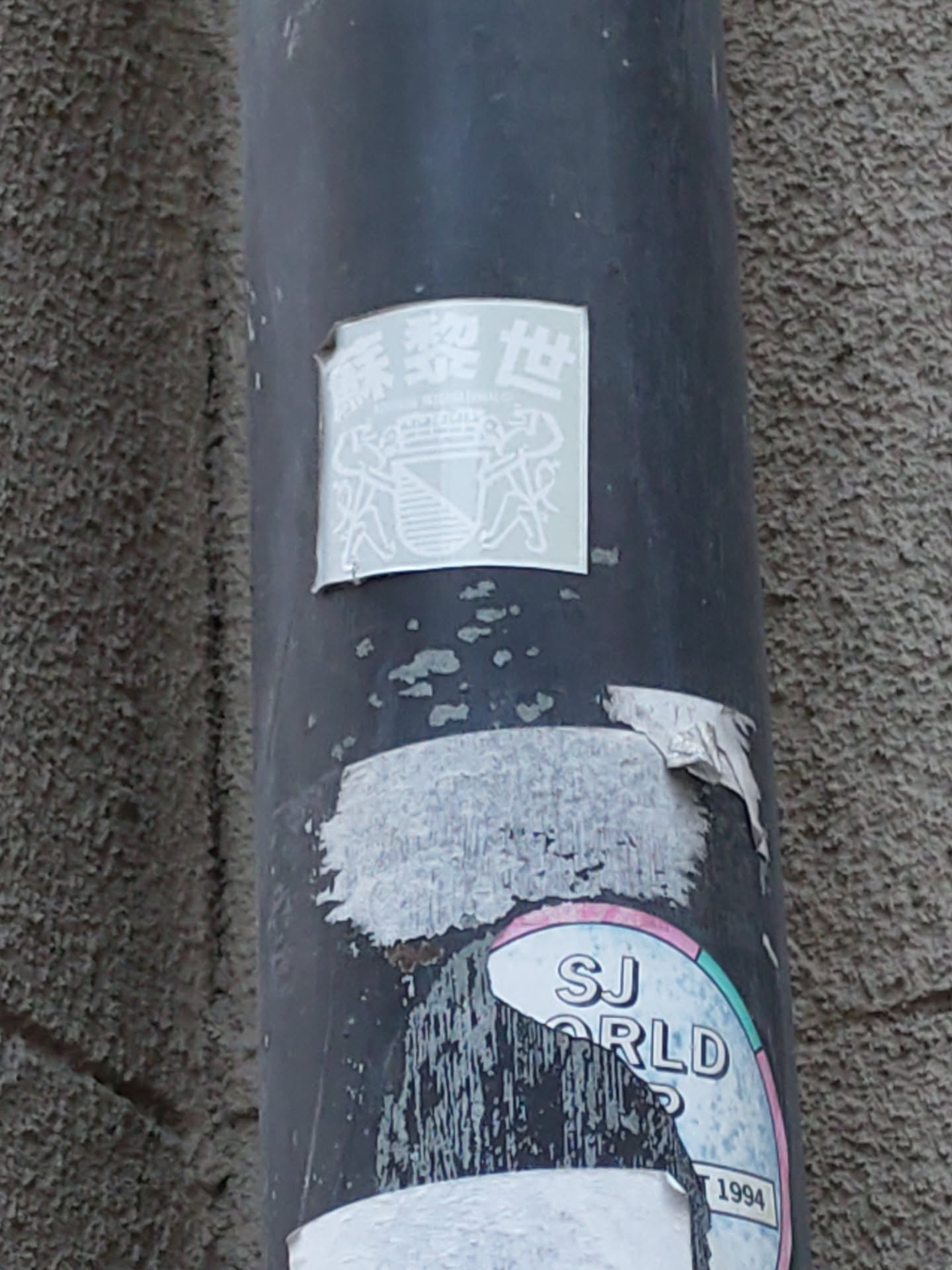 The sticker shows Chinese characters at the top, possibly indicating a name or place.  Below, there is an emblem resembling a crest, featuring what looks like a staircase within a shield.  The style is minimalist and simple, using only white ink on a transparent background.  The sticker is affixed to a dark gray pipe.