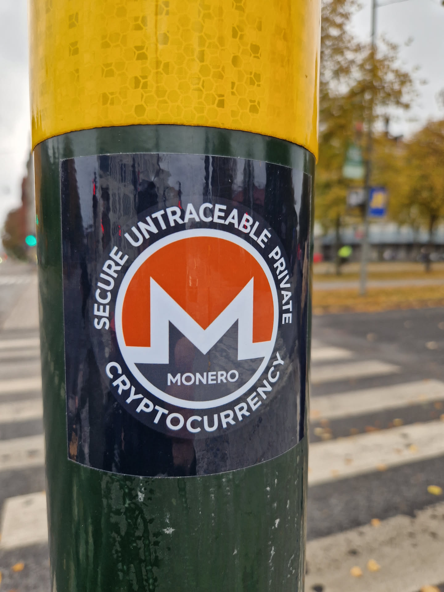 A Monero cryptocurrency sticker affixed to a pole. The sticker features the Monero logo and the words 'Secure Untraceable Private Cryptocurrency'.