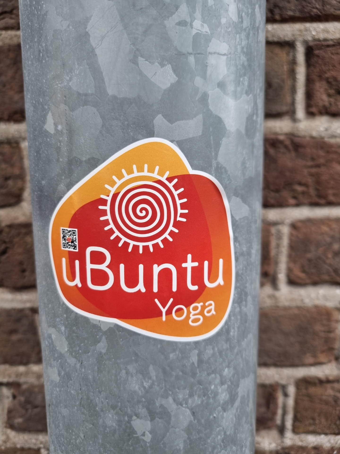 A red and orange sticker with the text "uBuntu Yoga" and an illustration of a sun with a spiral in the center.  There is a small QR code in the upper left corner of the sticker.