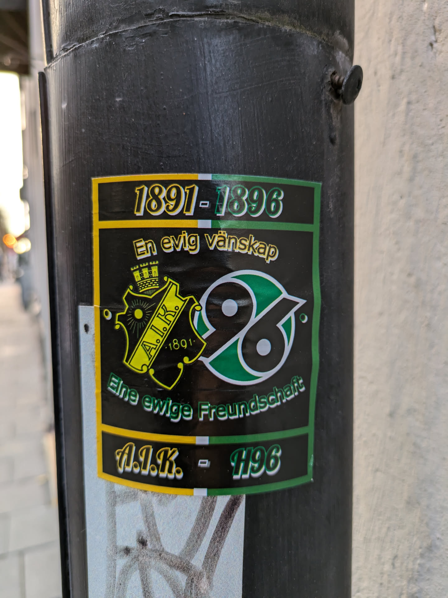 A sticker commemorating the friendship between AIK and Hannover 96, established in 1891. The sticker features the logos of both clubs and text in Swedish and German.