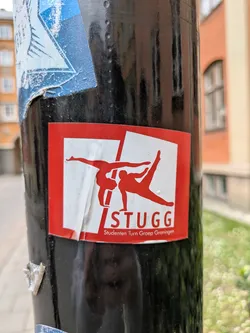 This is a sticker for STUGG, the student gymnastics group of Groningen. The design features two gymnasts in red silhouettes against a white background, set within a red square.