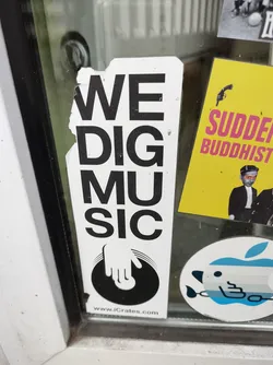 A sticker with the text 'WE DIG MUSIC' and an illustration of a hand on a vinyl record. The sticker has a website address at the bottom. 