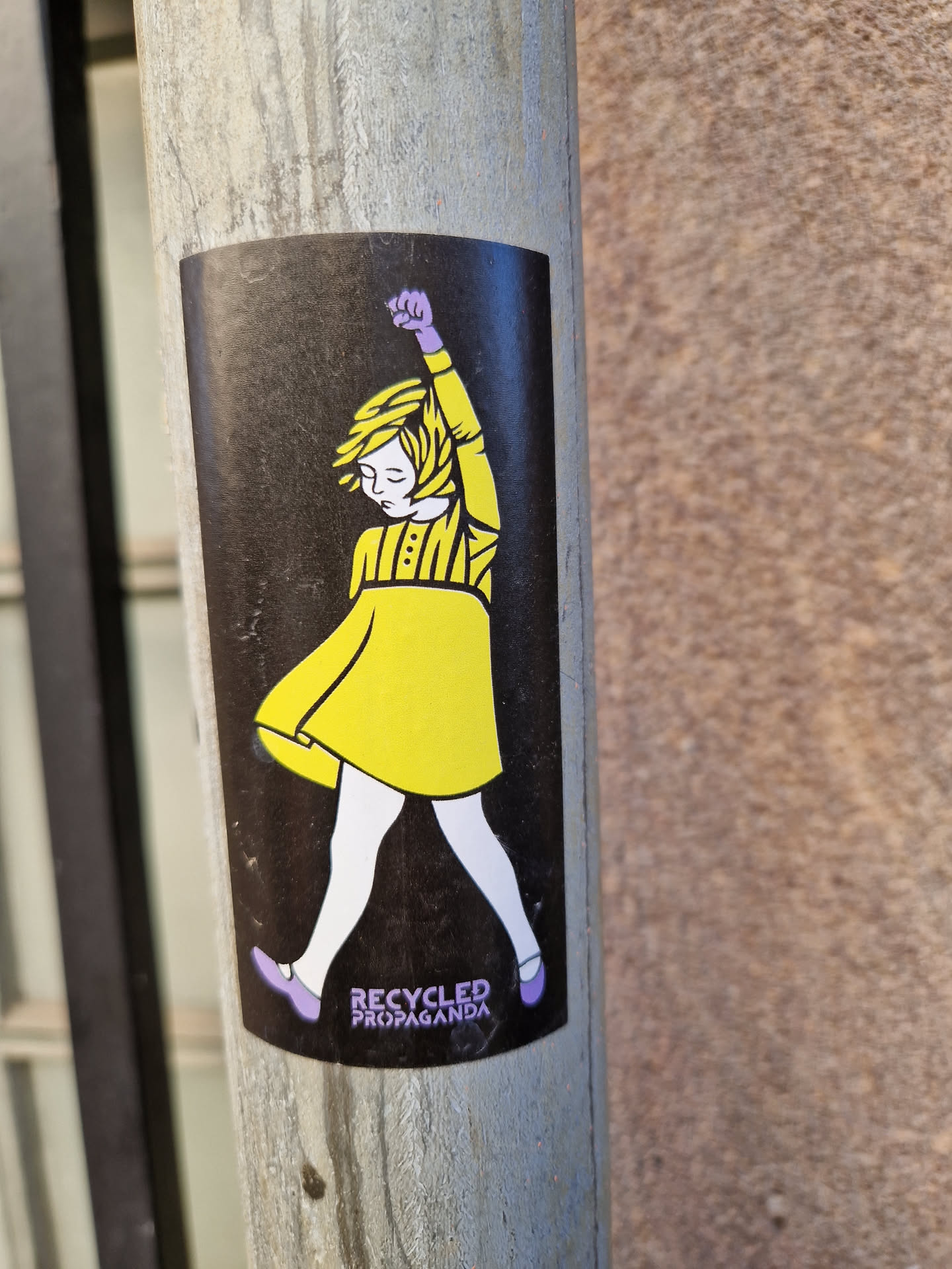 A sticker featuring a stylized illustration of a girl in a yellow dress, arm raised in a fist. The text 'Recycled Propaganda' is visible at the bottom.