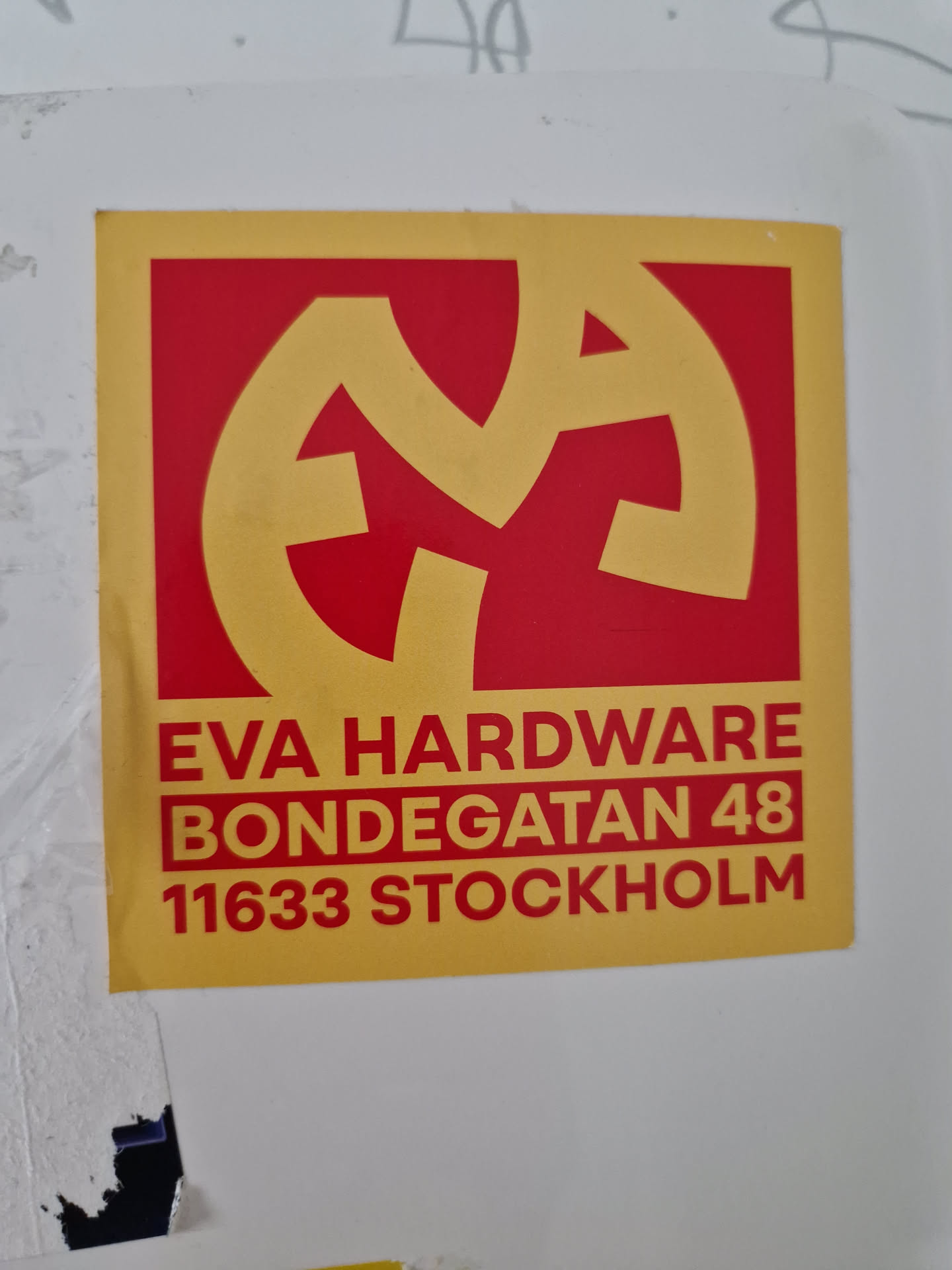 A yellow and red sticker with a logo and address information for Eva Hardware located in Stockholm, Sweden.