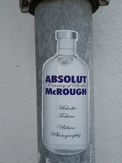 A sticker featuring an Absolut Vodka bottle with the text 'Absolut Country of Berlin McRough' and 'Melodic Techno Urban Photography' underneath. The sticker is affixed to a metallic pole.