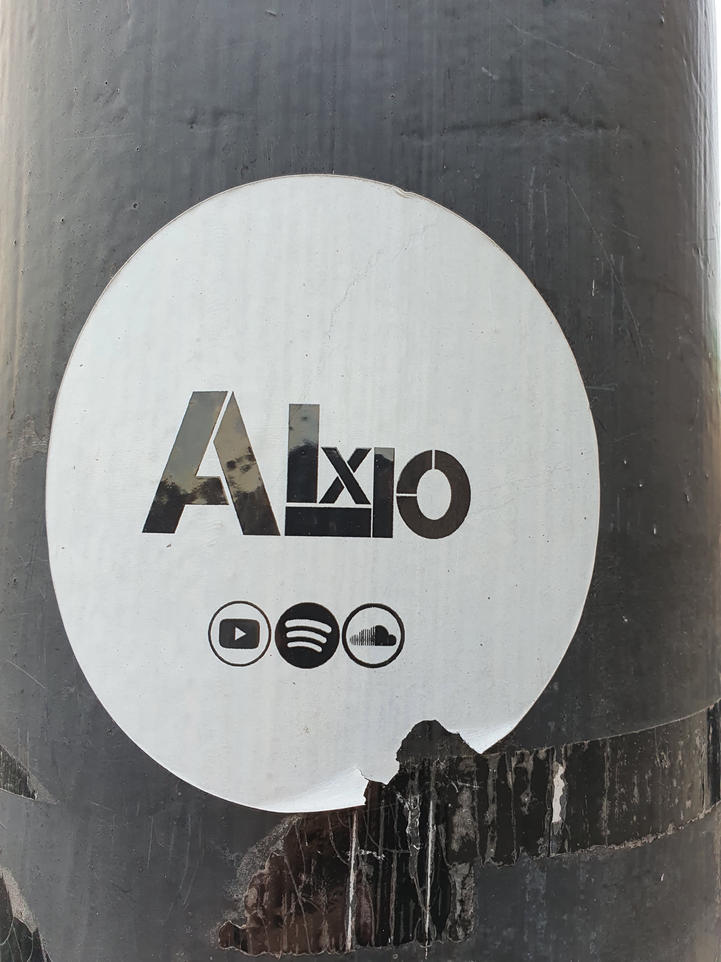 Round white sticker with the word Axio in a stylized font.  It includes links to the artist's YouTube, Spotify, and SoundCloud pages.