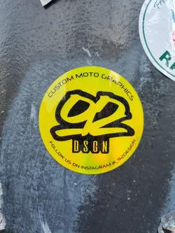 Round yellow sticker with black and glitter design. Contains the text "Custom Moto Graphics", a logo, "DSGN", and "Follow us on Instagram @92design".